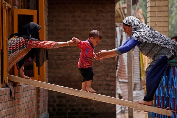 Mulheres ajudando uma criança a passar para outra casa por uma tábua de madeira após inundações nos arredores de Srinagar, Jammu e Caxemira, Índia. - Sputnik Brasil
