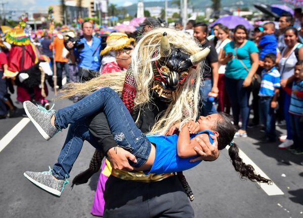 Pessoa com fantasia de uma criatura mitológica carregando uma menina durante uma parada em San Salvador - Sputnik Brasil
