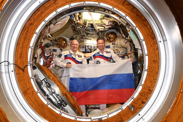 Astronautas russos Oleg Artemiev e Sergei Prokofiev segurando a bandeira da Rússia a bordo da Estação Espacial Internacional no Dia da Bandeira russa - Sputnik Brasil