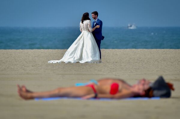 Casal de noivos ao fundo, enquanto pessoas tomam sol na praia em Deauville, França - Sputnik Brasil