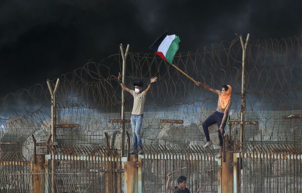 Manifestantes palestinos desfraldam bandeira na fronteira entre Israel e a Faixa de Gaza - Sputnik Brasil