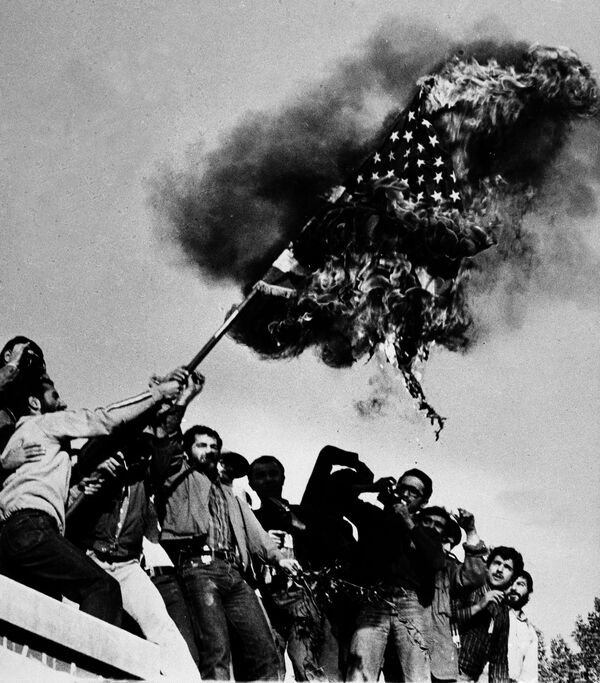 Manifestantes queimam a bandeira estadunidense no muro da embaixada dos EUA em Teerã na sequência da tomada de reféns em 4 de novembro, em 9 de novembro de 1979 - Sputnik Brasil