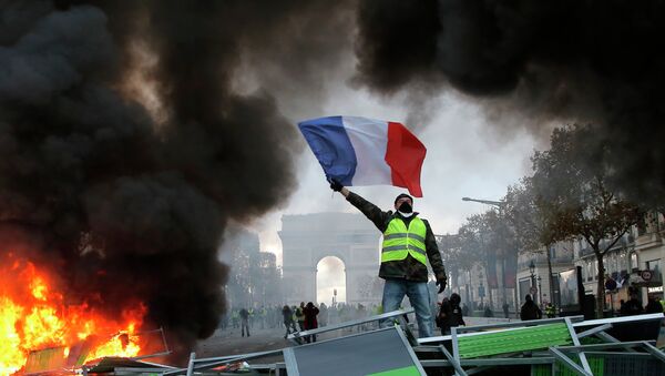 Um manifestante segura a bandeira da França sobre uma barricada em chamas na Avendia Champs-Elysees, com o arco do Triunfo ao fundo, durante a manifestação contra o aumento de combustíveis no país. Foto de 24 de novembro de 2018. - Sputnik Brasil