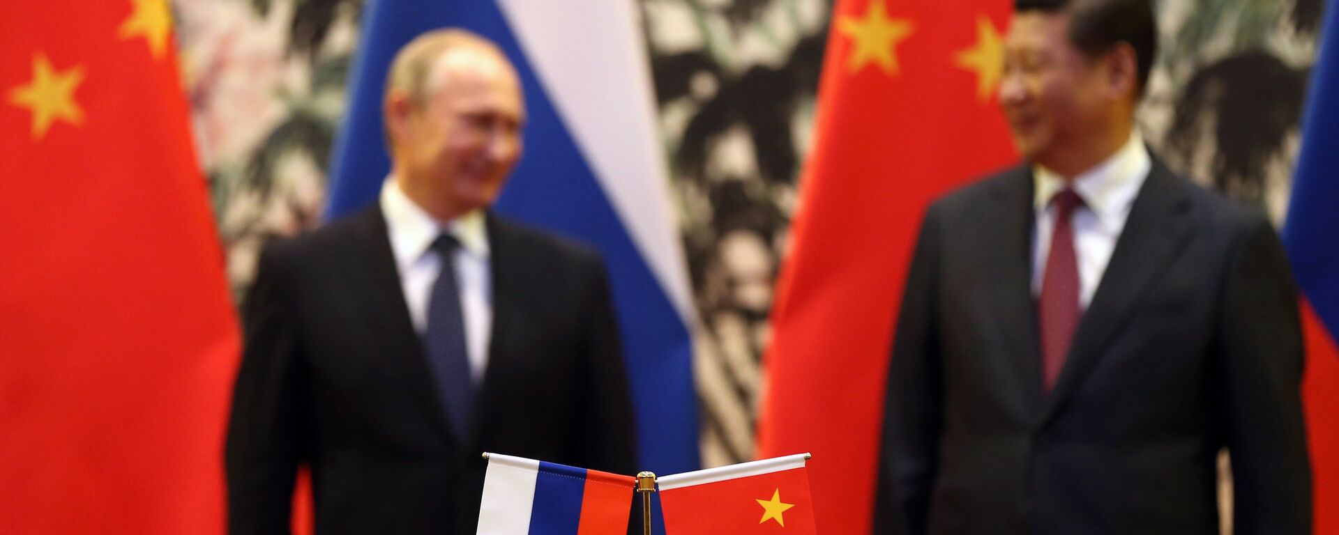 The Russian and Chinese national flags are seen on the table as Russia's President Vladimir Putin (back L) and his China's President Xi Jinping (back R) stand during a signing ceremony at the Diaoyutai State Guesthouse in Beijing on November 9, 2014. - Sputnik Brasil, 1920, 07.09.2022