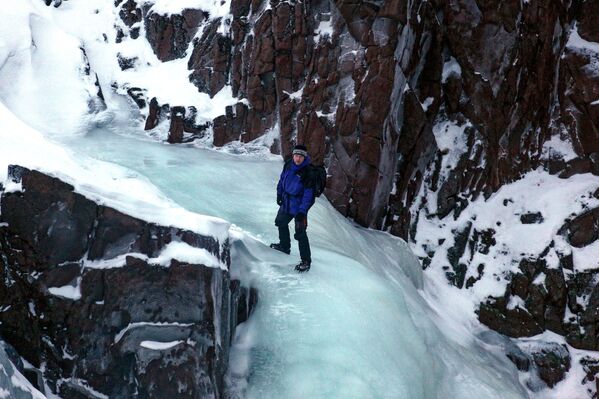 Turista escalando a cachoeira congelada, na península de Kola, na Rússia - Sputnik Brasil