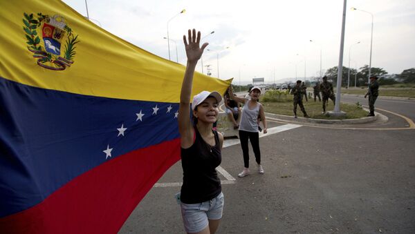 Mulher grita bem-vinda ajuda humanitária, balançando bandeira venezuelana em frente a grupo de soldados do Exército venezuelano e oficiais da Guarda Nacional bloqueando o acesso principal à ponte internacional Tienditas, que liga Colômbia e Venezuela, 7 de fevereiro de 2019 - Sputnik Brasil