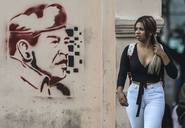 Mulher passa por muro com pichação do ex-presidente venezuelano Hugo Chávez, em Caracas, Venezuela, em 6 de fevereiro de 2019 - Sputnik Brasil