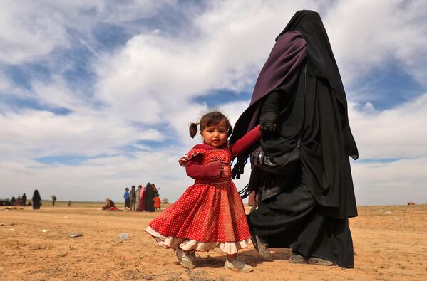 Mulher totalmente coberta caminha com filha enquanto civis, que fugiram do grupo do Estado Islâmico, reúnem-se em campo, em 13 de fevereiro de 2019 - Sputnik Brasil