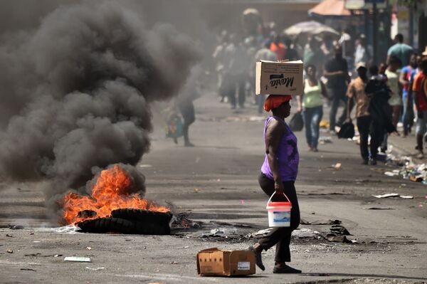 Uma mulher passa diante de pneu ardendo em uma rua de Porto Príncipe, capital do Haiti - Sputnik Brasil