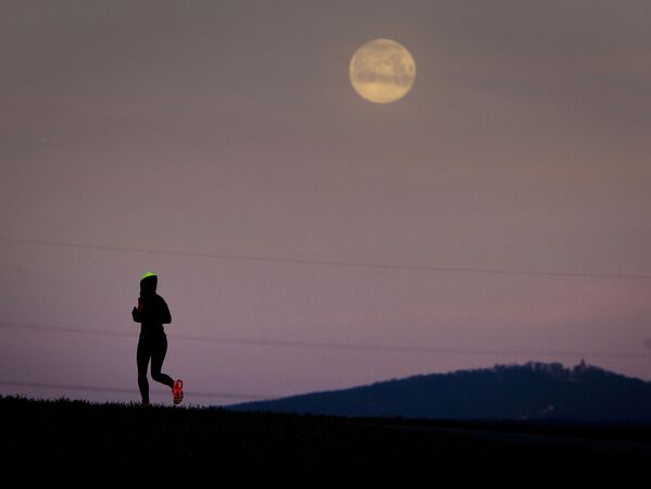 Uma jovem corre entre campos, antes de a Lua se pôr nos arredores de Frankfurt - Sputnik Brasil