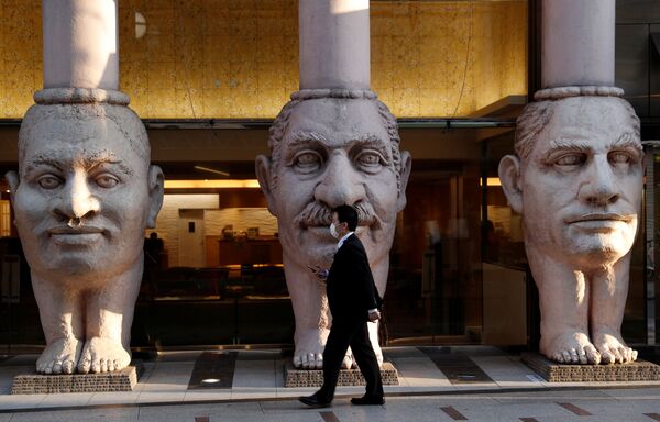 Homem caminha ao lado de colunas gigantescas feitas em forma de rostos humanos instaladas cerca do hotel Dotonbori em Osaka, Japão - Sputnik Brasil
