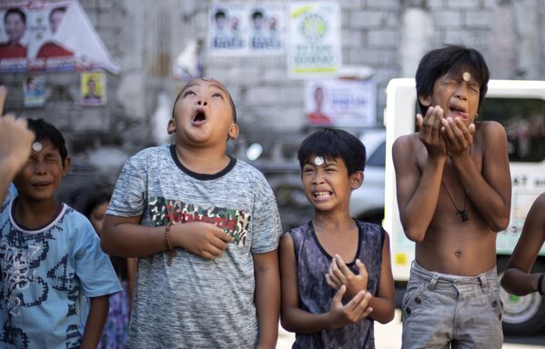 Meninos contorcem rosto enquanto participam de jogo em que precisam deslizar uma moeda da testa para a boca para vencer, durante a Festa de Santa Rita de Cássia, em Manila, 19 de maio de 2019 - Sputnik Brasil