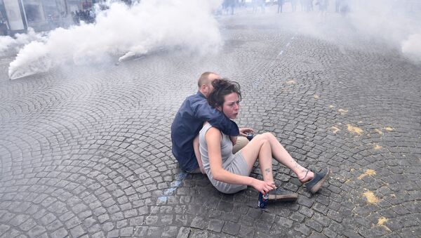 Um casal se protege em meio ao gás lacrimogêneo disparado pela polícia em confronto com manifestantes ligados ao movimento dos coletes amarelos após a tradicional parada militar do Dia da Bastilha em Paris - Sputnik Brasil