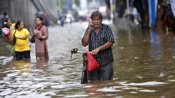 Um homem fala ao celular enquanto caminha em uma rua inundada devido às fortes chuvas em Mumbai, na Índia. - Sputnik Brasil