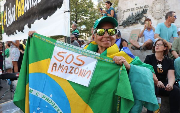 Manifestante com a bandeira do Brasil e cartaz SOS Amazônia durante ato contra queimadas na Amazônia em Lisboa, Portugal em 26 de agosto de 2019 - Sputnik Brasil
