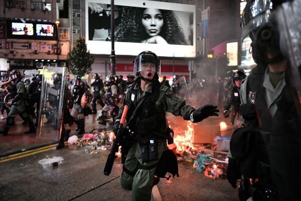 Polícia passa por destroços incendiados por manifestantes ao longo de uma rua em Hong Kong - Sputnik Brasil