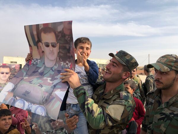 Crianças e militares seguram cartazes com a imagem do presidente da Síria, Bashar Assad, na cidade de Manbij, liberta pelo Exército sírio - Sputnik Brasil