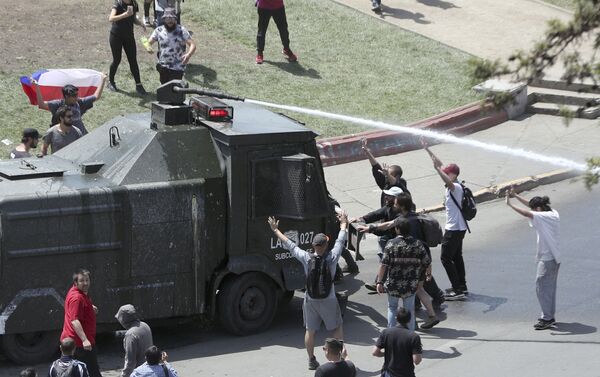 Manifestantes em Santiago, no Chile, confrontam um veículo policial equipado com canhões de água. O registro é do 5º dia de protestos de massa no país, em 22 de outubro de 2019. - Sputnik Brasil