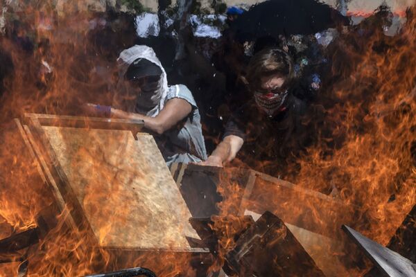 Manifestantes protegem o rosto contra bombas de gás lacrimogêneo e formam barricadas nas ruas de Santiago do Chile - Sputnik Brasil