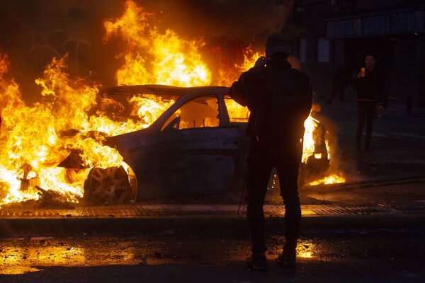 Chilenos observam carro queimado durante protestos contra o governo no Chile - Sputnik Brasil