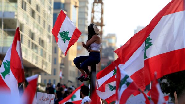 Manifestante sentada sobre um poste carregando uma bandeira do Líbano em Beirute durante protestos no dia 20 de outubro. - Sputnik Brasil