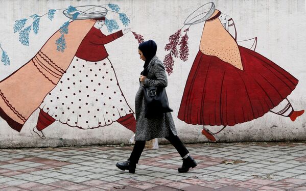 Mulher iraniana passa em frente a muro com desenho de mulheres camponesas do país - Sputnik Brasil