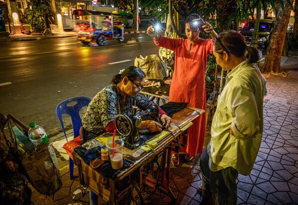 Mulher ilumina com celulares o local de trabalho de uma costureira de rua em Bangkok, Tailândia - Sputnik Brasil