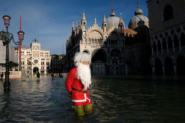 Homem vestido de Papai Noel com botas impermeáveis caminha pela praça de San Marco, na cidade italiana de Veneza, durante inundação provocada pela maré - Sputnik Brasil