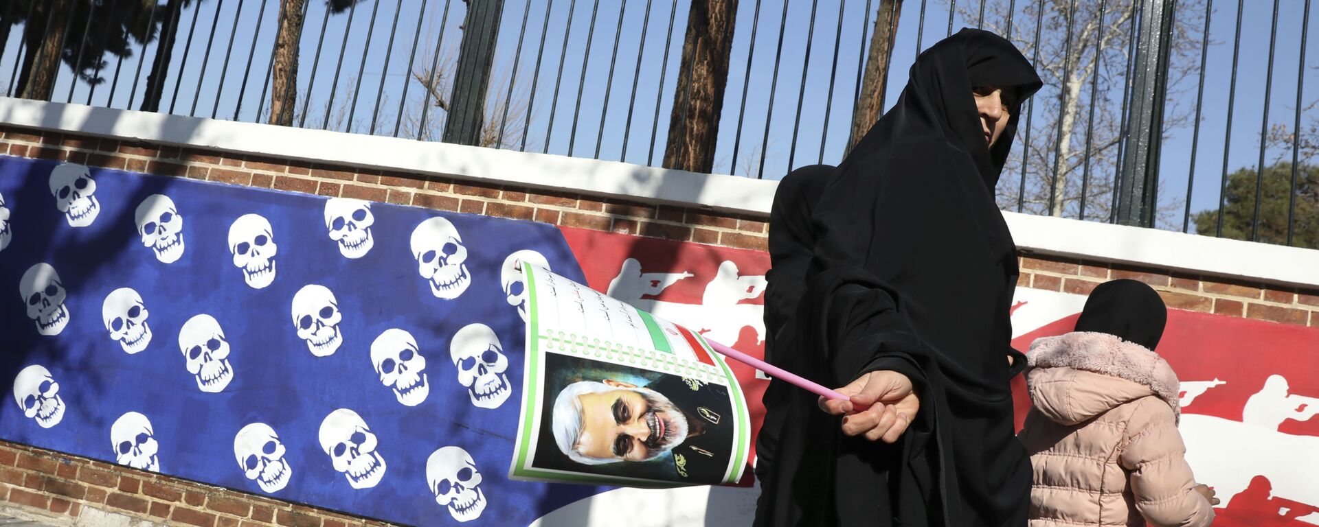 Mulher iraniana caminha com retrato do general Qassem Soleimani perto de muro com representação de bandeira dos Estados Unidos - Sputnik Brasil, 1920, 03.01.2023
