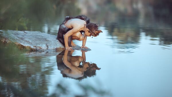 Menino da época dos homens das cavernas sentado na rocha e olhando para o seu próprio reflexo na água do lago. Conceito de sobrevivência de evolução. Foto de arte criativa - Sputnik Brasil