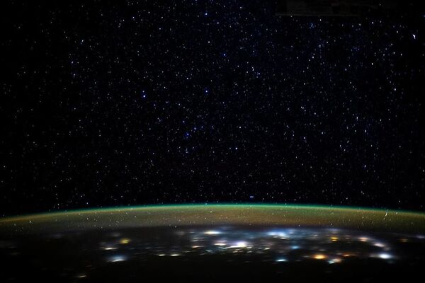 Estrelas brilhando por cima da camada de luz formada pela atmosfera da Terra, enquanto a Estação Espacial Internacional orbita a cerca de 400 km sobre a Terra - Sputnik Brasil
