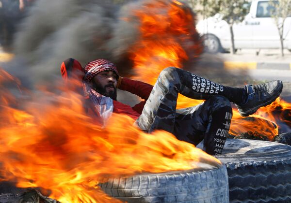 Manifestante iraquiano senta entre pneus em chamas tentando bloquear uma via pública durante protesto antigovernamental em Najaf, Iraque - Sputnik Brasil