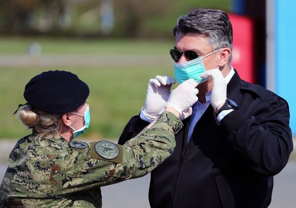 Soldado ajuda o presidente da Croácia, Zoran Milanovic, a colocar a máscara facial para se proteger contra coronavírus no hospital Dubrava em Zagreb, Croácia, 21 de março de 2020 - Sputnik Brasil
