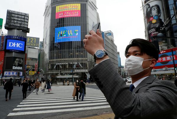 Homem com máscara para se proteger do coronavírus tira uma foto ao meio-dia, em Tóquio, Japão - Sputnik Brasil