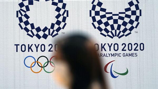 Mulher com máscara passa diante de logo das Olimpíadas de Tóquio, em 1º de abril de 2020 - Sputnik Brasil
