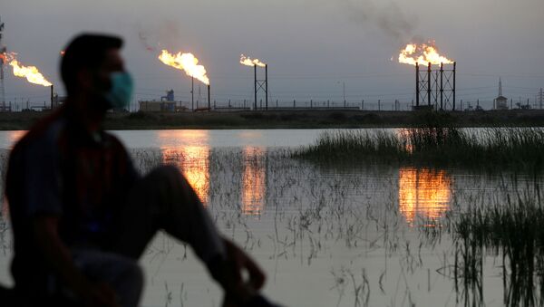 Chamas saem de torres de extração no campo petrolífero de Nahr Bin Umar, sendo visto um homem usando máscara facial protetora, após o surto do coronavírus, ao norte de Basra, Iraque - Sputnik Brasil
