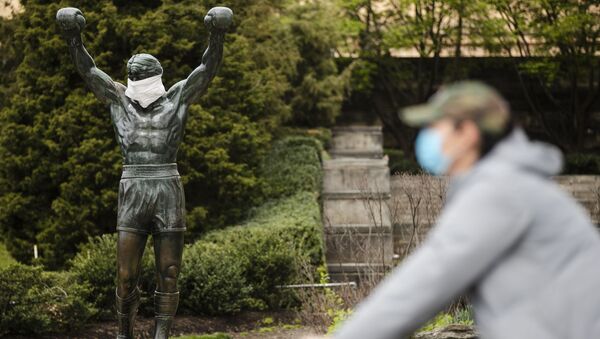 Ciclista usando máscara protetora passa pela estátua dedicada ao personagem Rocky, no Museu de Arte de Filadélfia, nos EUA, 14 de abril de 2020 - Sputnik Brasil