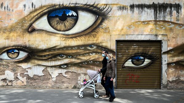 Casal usando máscaras e empurrando carrinho de bebê passa por muro grafitado em Roma, Itália, 13 de abril de 2020 - Sputnik Brasil
