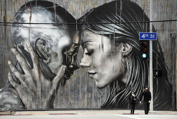 Casal com máscaras passam em frente a muro grafitado em um bairro em Los Angeles, Califórnia, EUA, 10 de abril de 2020 - Sputnik Brasil