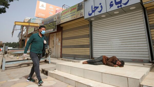 Um homem iraquiano usando máscara e luvas caminha em Basqa, no Iraque, ao lado de homem em situação de rua, que dorme em frente a uma loja durante toque de recolher imposto pelo governo para conter a pandemia do novo coronavírus. - Sputnik Brasil