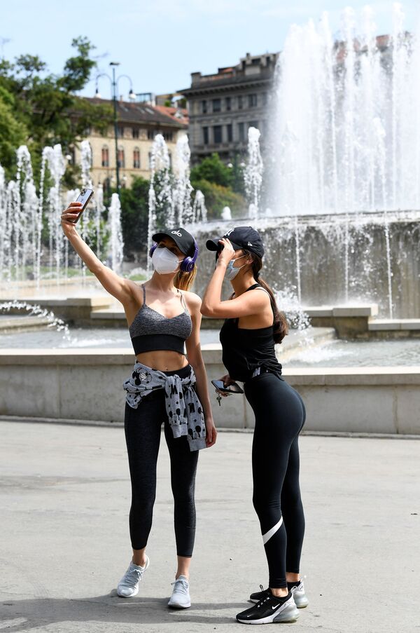 Moças fazem selfie usando máscaras tendo como fundo o chafariz na praça Castello, em Milão, Itália - Sputnik Brasil