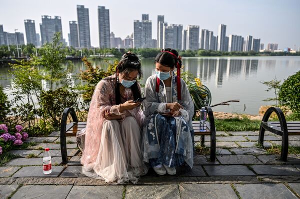 Mulheres vestindo máscaras e trajes tradicionais sentadas em banco em Wuhan, na província de Hubei, centro da China, em 17 de maio de 2020 - Sputnik Brasil
