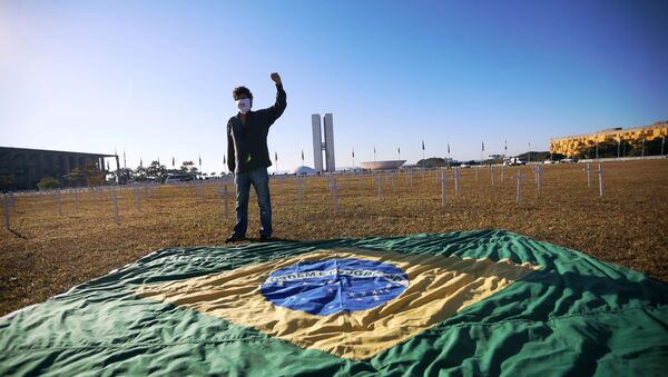 Ativista ao lado da bandeira brasileira e de cruzes simbolizando os que morreram por COVID-19, em frente ao Congresso Nacional, Brasília, Brasil, 28 de junho de 2020 - Sputnik Brasil