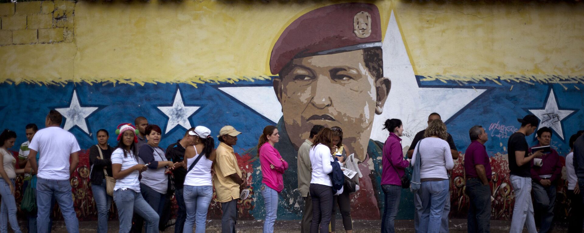 Venezuelanos fazem fila para participar das eleições em seu país em frente a muro com a imagem do ex-presidente Hugo Chávez - Sputnik Brasil, 1920, 17.04.2024