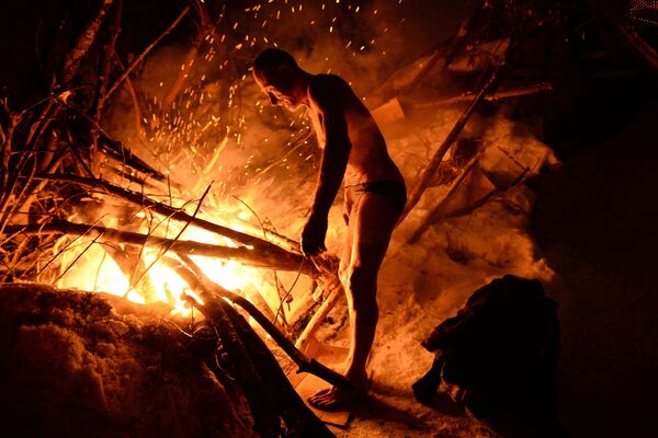 Homem se esquenta em fogueira após realizar mergulho de batismo em água gelada, em Novosibirsk - Sputnik Brasil