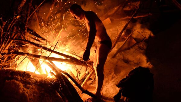 Homem se esquenta em fogueira após realizar mergulho de batismo em água gelada, em Novosibirsk - Sputnik Brasil