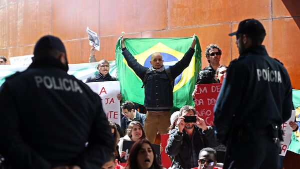 Polícia olha para um manifestante que se cobre com uma bandeira do Brasil e outros que mostram cartazes pró-democracia durante a conferência na Universidade de Lisboa em 31 de março - Sputnik Brasil