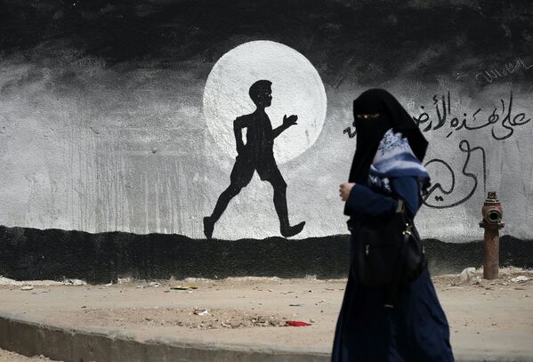 Uma mulher palestina passa por um grafite pintado na parede da escola das Nações Unidas, na Faixa de Gaza - Sputnik Brasil