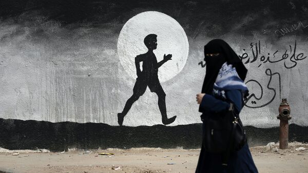 Uma mulher palestina passa por um grafite pintado na parede da escola das Nações Unidas, na Faixa de Gaza - Sputnik Brasil