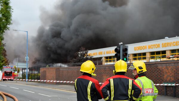 Firefighters stand beside a cordon as they tend to a fire at a recycling plant in Smethwick near Birmingham - Sputnik Brasil